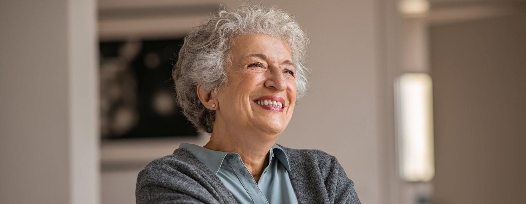 elderly woman with a cane, sits in a room and smiles