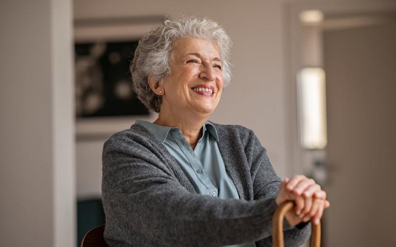 elderly woman with a cane, sits in a room and smiles